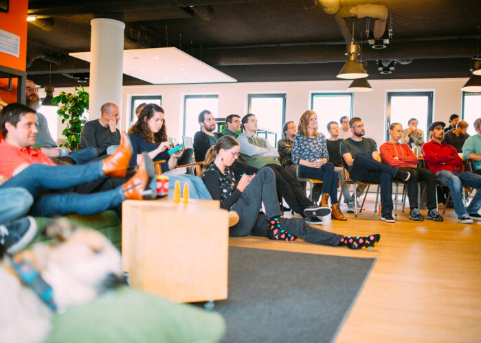 Groep mensen die naar iets kijkt (buiten beeld), casual zittend in een kantoor-setting