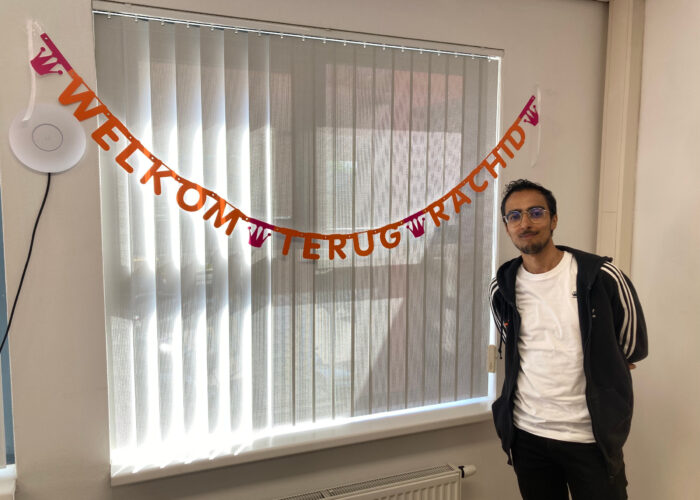 Lachend persoon naast een slinger met letters "Welkom terug Rachid"