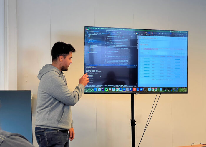 Person standing in front of a monitor showing some code and a browser window.