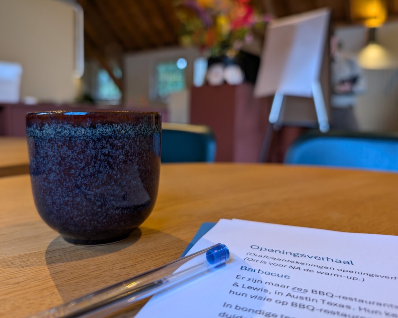 Close up van een kop koffie, wat tekst, en een kleurijke ruimte blurry op de achtergrond