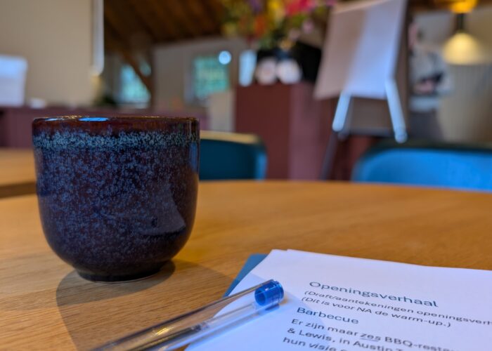 Close up van een kop koffie, wat tekst, en een kleurijke ruimte blurry op de achtergrond